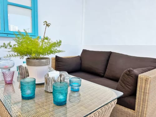 Terraza moderna en Fuengirola con muebles de mimbre, cojines oscuros, toques turquesas, plantas y vistas a la ciudad