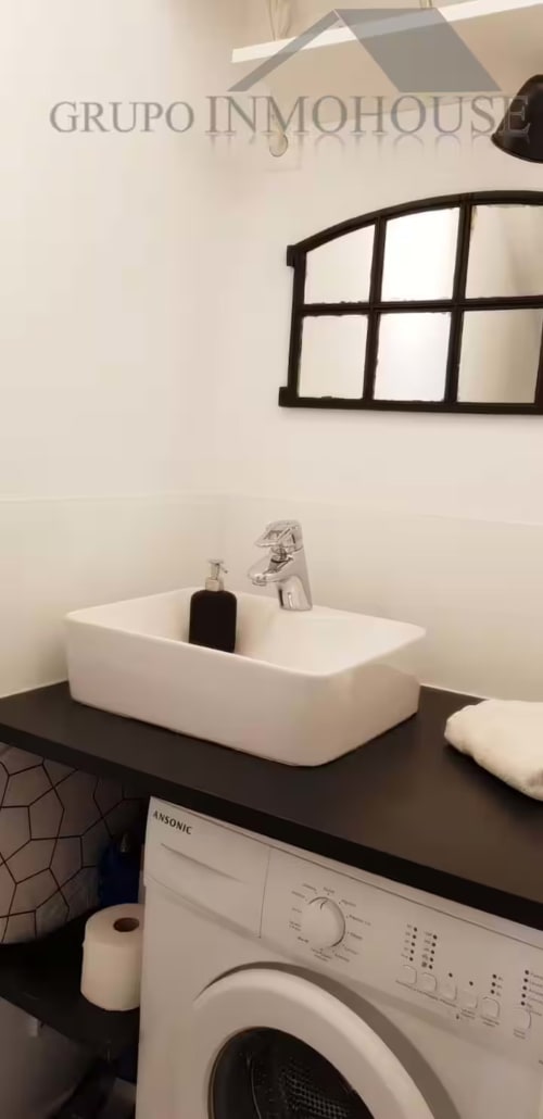 Moderno lavabo de baño con lavamanos blanco, espejo negro y lavadora en apartamento de Fuengirola