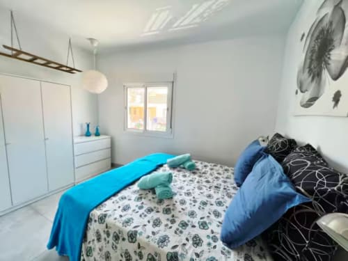 Dormitorio luminoso en apartamento de Fuengirola con detalles azules, muebles blancos y ropa de cama floral