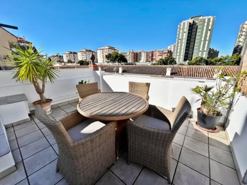 Terraza en la azotea con sillas de mimbre, mesa redonda y vistas a la ciudad en apartamento de Fuengirola