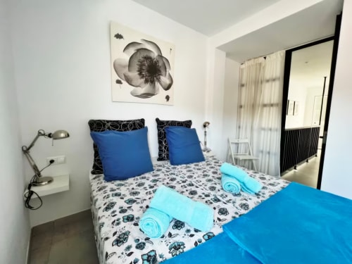 Dormitorio moderno en apartamento de Fuengirola con almohadas azules, ropa de cama estampada, toallas enrolladas y cuadros en paredes blancas