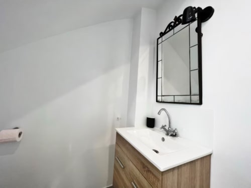 Moderno lavabo de baño con vanidad blanca, espejo con marco negro y grifo cromado en apartamento de Fuengirola