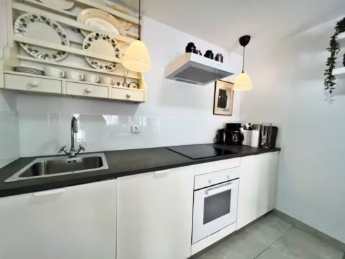 Cocina moderna en apartamento de Fuengirola con muebles blancos, encimera negra, lámparas colgantes y acero inoxidable