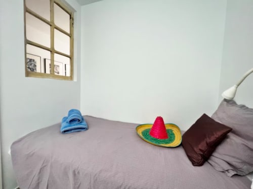 Acogedora habitación de apartamento en Fuengirola con ropa de cama gris, toalla azul, sombrero decorativo y espejo de madera en paredes blancas