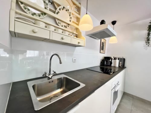 Cocina moderna en apartamento de Fuengirola con fregadero de acero inoxidable, encimera oscura, muebles blancos e iluminación colgante