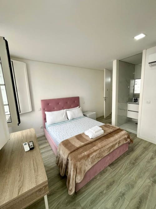 Modern Suite A at Casa Augusta hostel in Braga, featuring pink headboard bed, en-suite bathroom, wood flooring