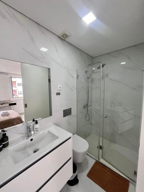 Modern bathroom at Casa Augusta hostel in Braga with marble walls, white sink, toilet, and glass shower enclosure