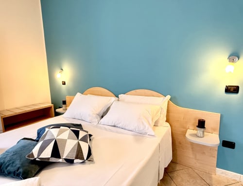 Camera luminosa all'Hotel Il Mulino con pareti blu, letto in legno, cuscini bianchi e moderni sistemi di illuminazione