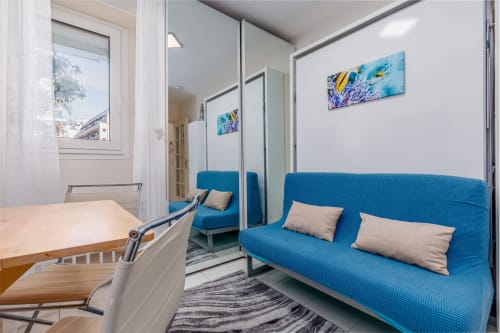 Appartement moderne Riviera Home avec canapé bleu, mur miroir, lumière naturelle et vue sur la ville à Roquebrune-Cap Martin