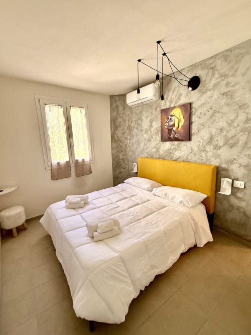 Chambre moderne à BB Sassuolo avec tête de lit jaune, murs en marbre, luminaires suspendus et literie blanche