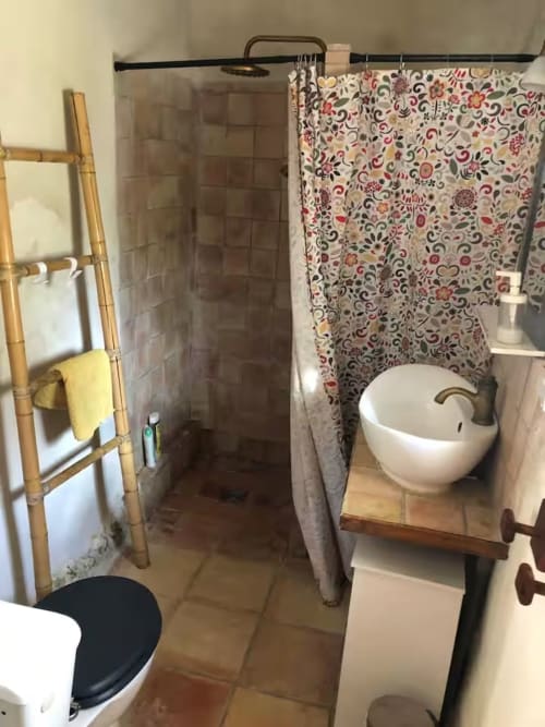 Salle de bain du cottage de la Bastide Saint Michel avec rideau de douche à motifs, lavabo rond et échelle porte-serviettes en bois