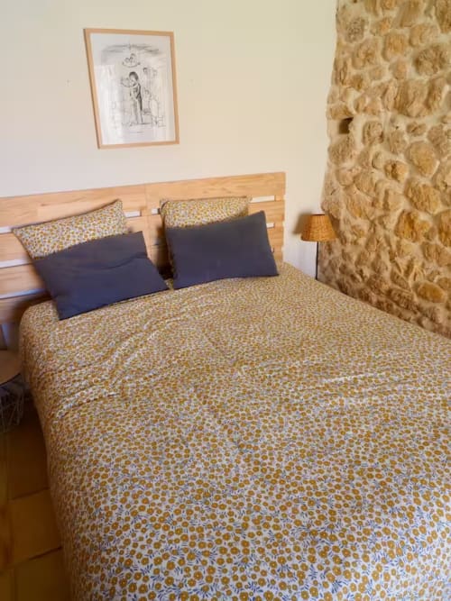 Chambre accueillante à la Bastide Saint Michel avec parure florale, tête de lit en bois et mur en pierre au gîte Le Tournesol