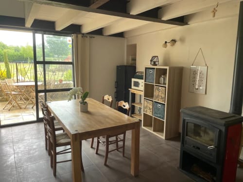 Salle à manger ouverte de la Bastide Saint Michel avec table en bois, cheminée, étagères de rangement et portes sur jardin