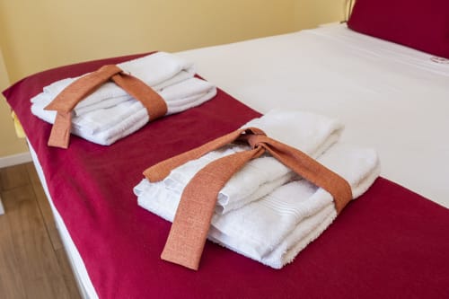 Rolled white towels with terracotta bands arranged on burgundy bedspread in RH Charming Apartment Liberdade II, Braga