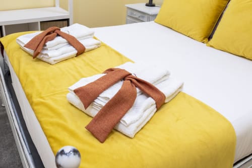 Two beds with yellow bedding and white pillows at RH Charming Apartments in Braga, with brown towels rolled on mattresses