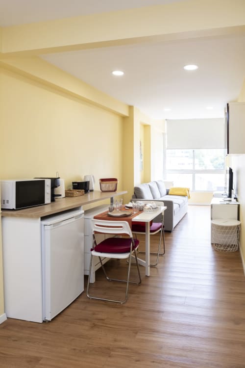 Modern apartment living space at RH Charming Apartments Braga with yellow walls, kitchenette, dining table, gray sofa, and