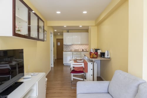 Modern studio apartment in Braga with yellow walls, kitchen, dining area, sofa, and wooden flooring at RH Charming Apartments