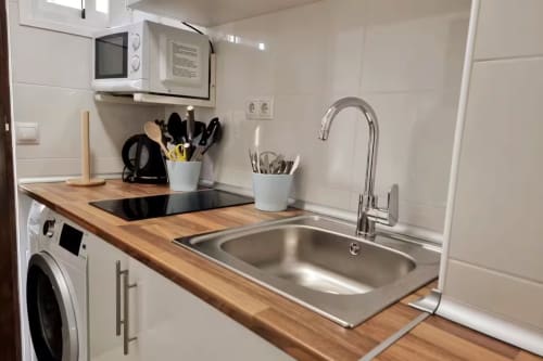 Cocina moderna en estudio de Fuengirola con encimeras de madera, fregadero de acero inoxidable, placa de cocción, microondas y lavadora