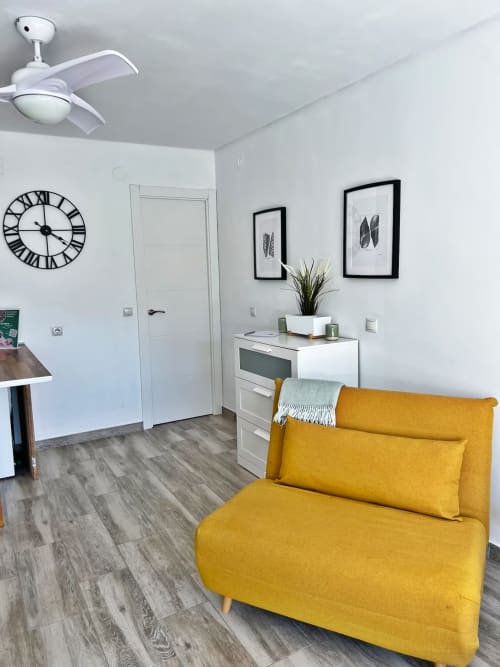 Moderno estudio en Fuengirola con sofá amarillo, cocina blanca, ventilador de techo y decoración minimalista