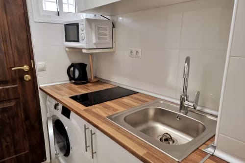 Moderna cocina estudio en Fuengirola con encimera de madera, fregadero acero inoxidable, placa cocción, microondas y lavadora