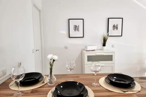 Comedor moderno ambientado para tres personas con platos negros, copas de vino y flores blancas en apartamento de Fuengirola