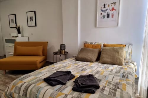 Moderno apartamento estudio en Fuengirola con silla naranja, cama con ropa de cama estampada y arte de insectos en las paredes