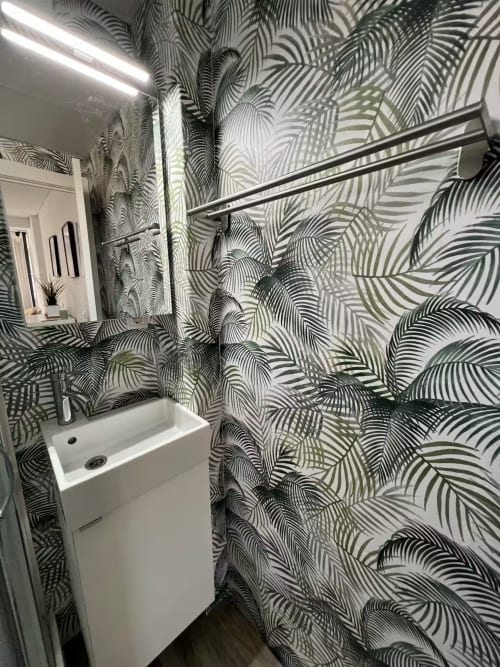 Baño moderno en apartamento de Fuengirola con papel tapiz de hojas tropicales, lavabo blanco, espejo e iluminación lineal