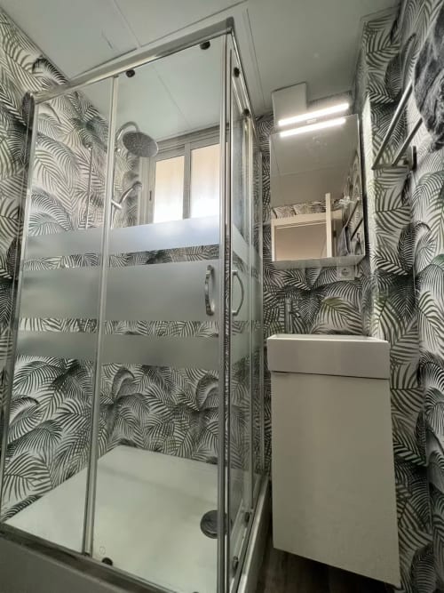 Baño moderno con papel mural efecto cebra, mampara de ducha de cristal y lavabo blanco en apartamento nuevo de Fuengirola