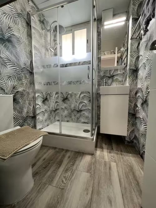 Baño moderno en estudio nuevo de Fuengirola con paredes de rayas cebra, ducha de cristal y piso efecto madera