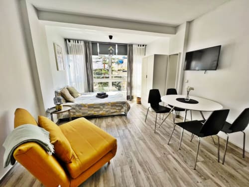 Moderno apartamento estudio en Fuengirola con asientos amarillos, comedor, cama, TV y vistas a la ciudad desde balcón