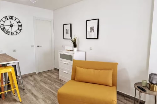Moderno estudio en Fuengirola con sillón amarillo, muebles blancos y comodidades urbanas
