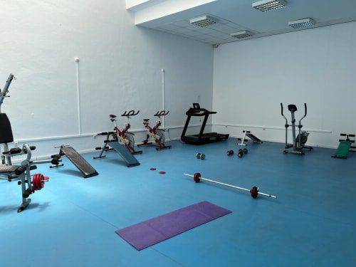 Moderno estudio de fitness en Grupo Inmo House, Fuengirola con equipos cardiovasculares, pesas y tapete de yoga sobre piso azul