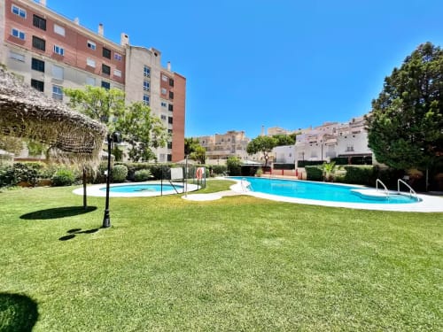 Complejo de apartamentos en Fuengirola con piscina, jardín verde y vista a edificios de la ciudad bajo cielo despejado
