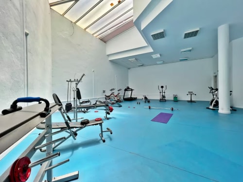 Moderno estudio de fitness con suelo azul, equipos de ejercicio y claraboya en apartamento de Fuengirola