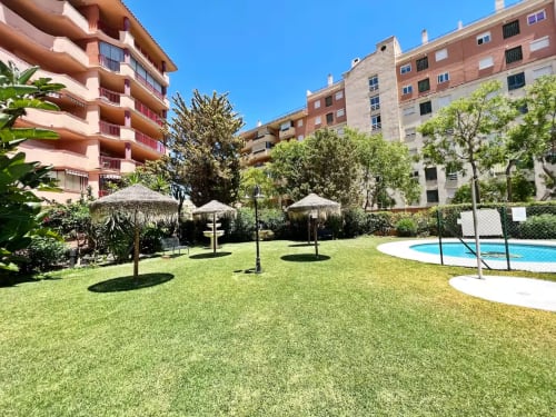 Patio de apartamento en Fuengirola con piscina, jardín y edificios modernos bajo un cielo azul despejado