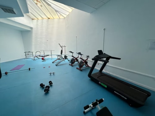 Moderno estudio de fitness en apartamento de Fuengirola con cinta de correr, bicicletas estáticas, pesas y colchoneta de yoga sobre piso azul