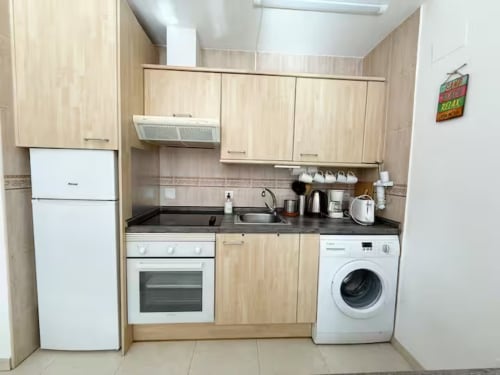 Cocina moderna en estudio de Fuengirola con muebles de madera clara, electrodomésticos blancos y distribución compacta