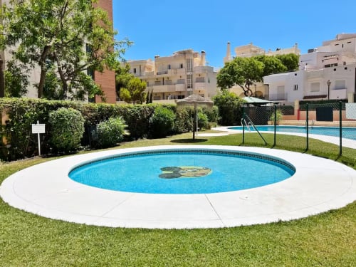 Piscina circular con tumbonas en el complejo de apartamentos Grupo Inmo House en Fuengirola, rodeada de césped y vegetación mediterránea