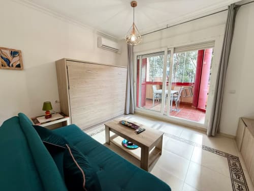 Luminoso estudio en Fuengirola con sofá turquesa, cama abatible, muebles de madera y acceso a patio desde balcón