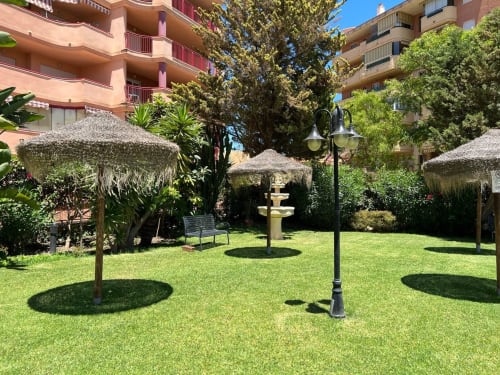 Patio del hotel en Fuengirola con sombrillas, césped cuidado, fuente y edificios residenciales