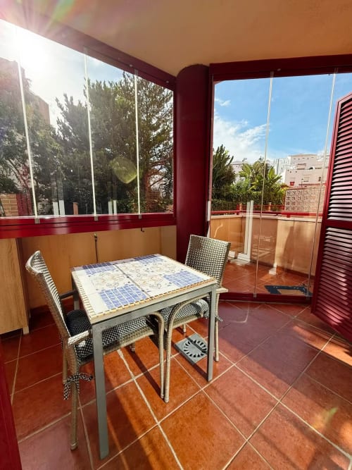 Terraza soleada del apartamento Grupo Inmo House Fuengirola con mesa de comedor, sillas de ratán y vistas a la ciudad