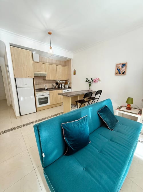 Luminoso apartamento estudio en Fuengirola con sofá turquesa, cocina abierta, armarios de madera y amenidades modernas