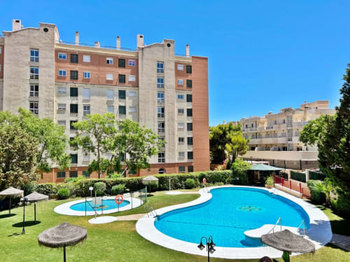 Complejo de apartamentos en Fuengirola con piscinas curvas, piscina infantil y jardines cuidados bajo cielo despejado
