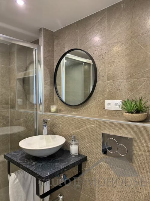 Baño moderno en apartamento de playa en Fuengirola con espejo redondo, lavamanos tipo vasija y acabados en piedra