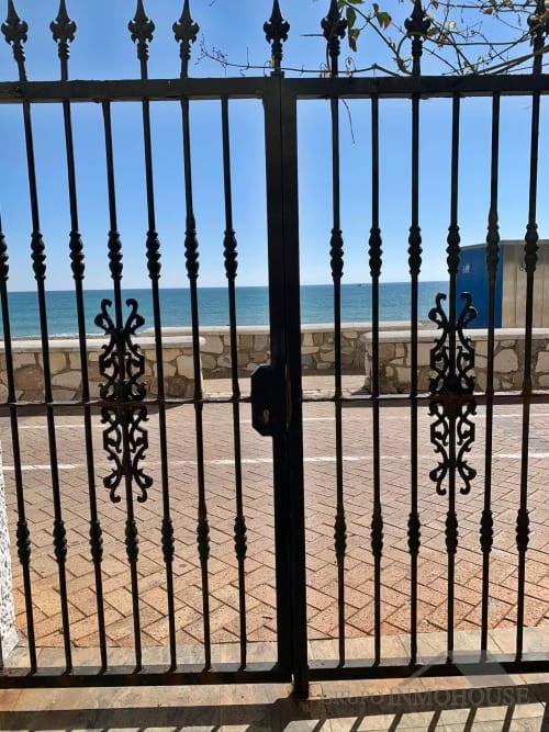 Ornada puerta de hierro negro que abre a la playa de Fuengirola con vistas al mar y terraza arenosa