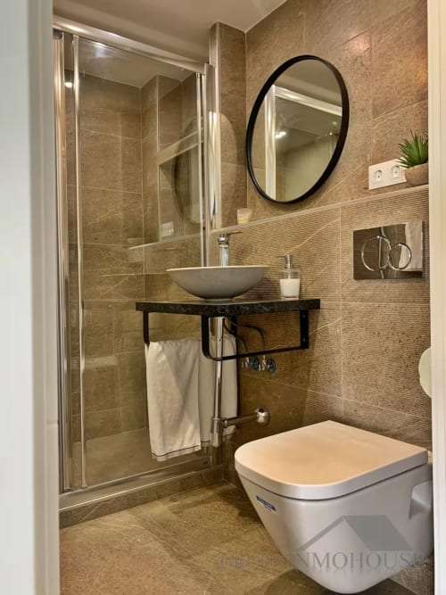 Baño moderno en apartamento de Fuengirola con ducha a ras de suelo, lavamanos tipo vasija, espejo redondo y elegancia costera