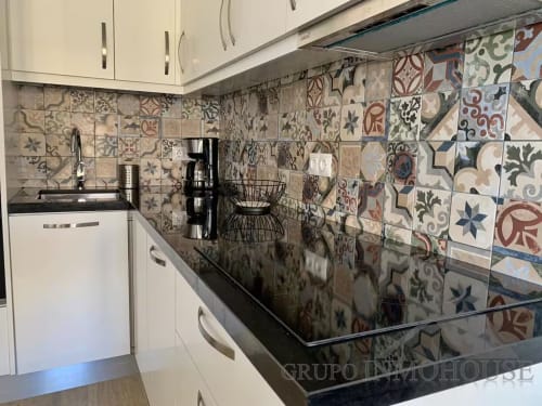 Cocina moderna con azulejos estampados, muebles blancos y encimera negra en apartamento playa de Fuengirola