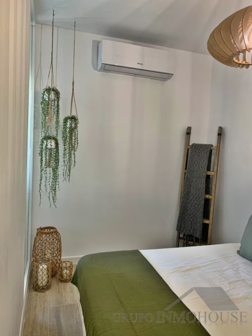 Dormitorio moderno de apartamento en playa de Fuengirola con vistas al mar, ropa de cama verde, plantas colgantes y decoración minimalista