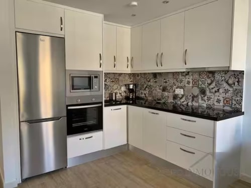 Cocina moderna con gabinetes blancos, electrodomésticos de acero inoxidable, encimera negra y azulejos decorativos en Fuengirola
