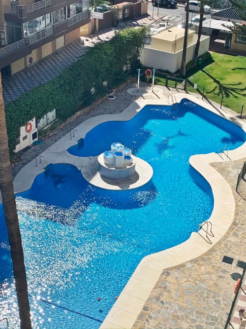 Piscina resort azul brillante con área central de jacuzzi con vistas al mar Mediterráneo en Fuengirola, España